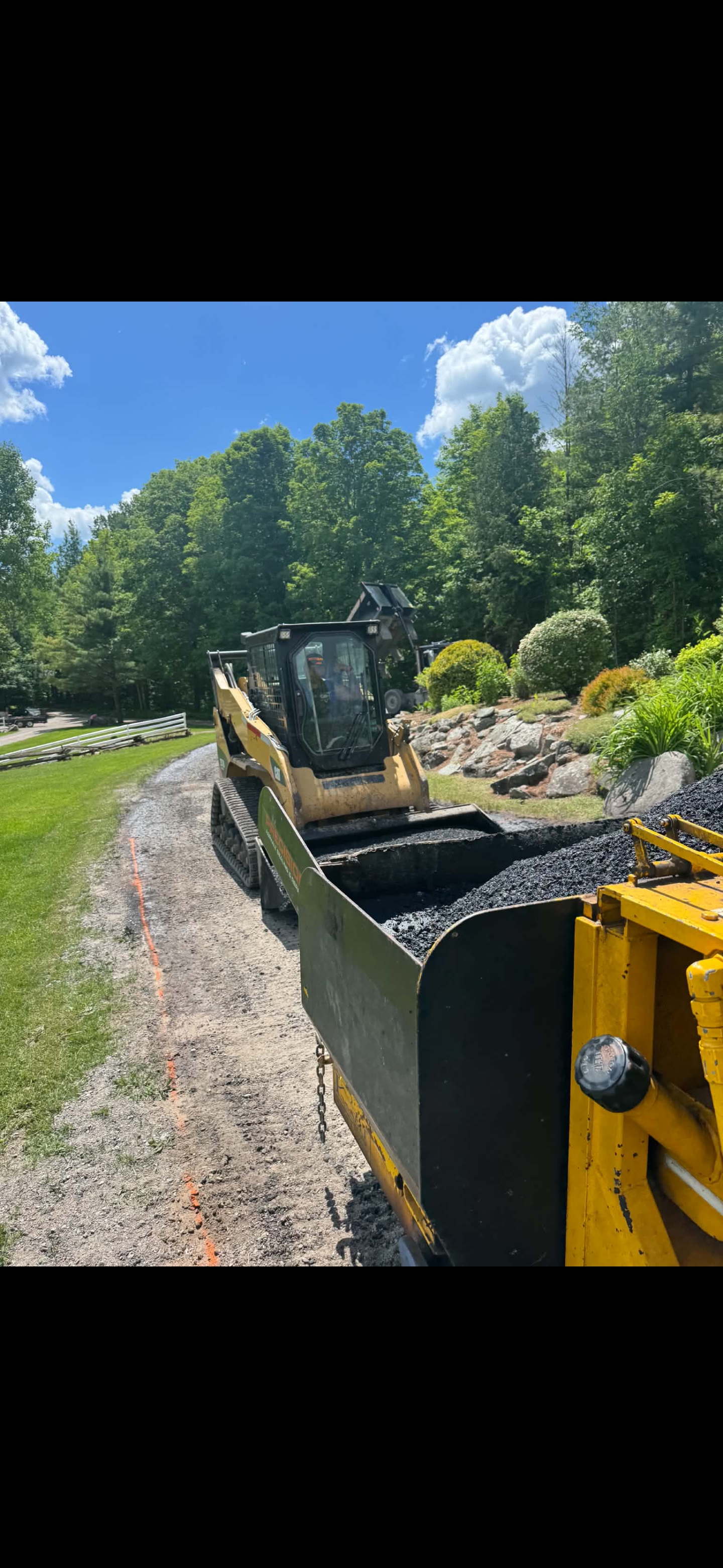 Skid steer loading asphalt into commercial paver box